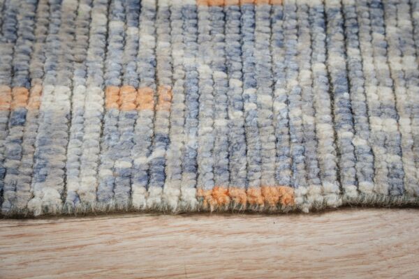 Close-up of a high-pile, textured rug featuring abstract blocks of blue, cream, and orange on light wood flooring.