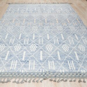 Textured blue and white geometric rug with fringe and peach accents rests on a blonde wood floor.