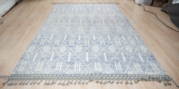 Textured blue and white geometric rug with fringe and peach accents rests on a blonde wood floor.