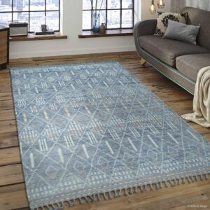 Blue rug with geometric white and orange patterns and fringe on wide plank wooden flooring.