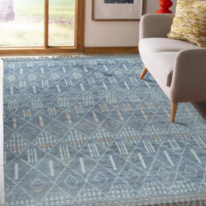 Blue textured rug with geometric white and orange accents near a neutral armchair and sunny window.