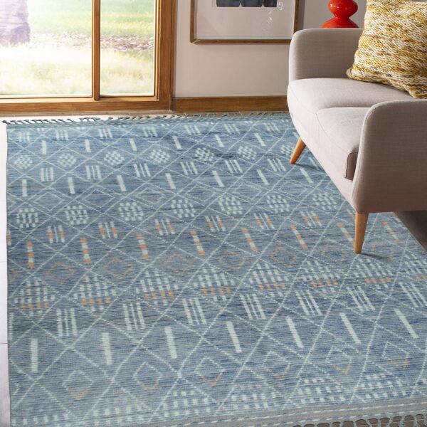 Blue textured rug with geometric white and orange accents near a neutral armchair and sunny window.