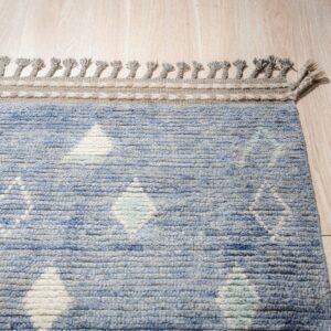 Textured blue rug featuring diamond patterns, a gray border, and braided tassels on light wood planks.
