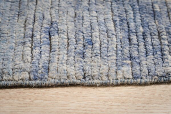Textured blue and cream high pile rug with pronounced vertical rows rests on light wood grain.