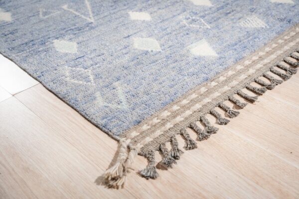 Chunky blue rug with cream geometric patterns and gray fringe rests on light blonde wood flooring.