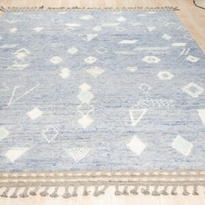 Textured light blue rug with scattered white geometric patterns and gray braided tassels on a light wood floor.