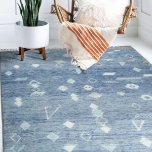 A blue rug with white and teal geometric patterns lies beneath a wicker chair and potted plant.