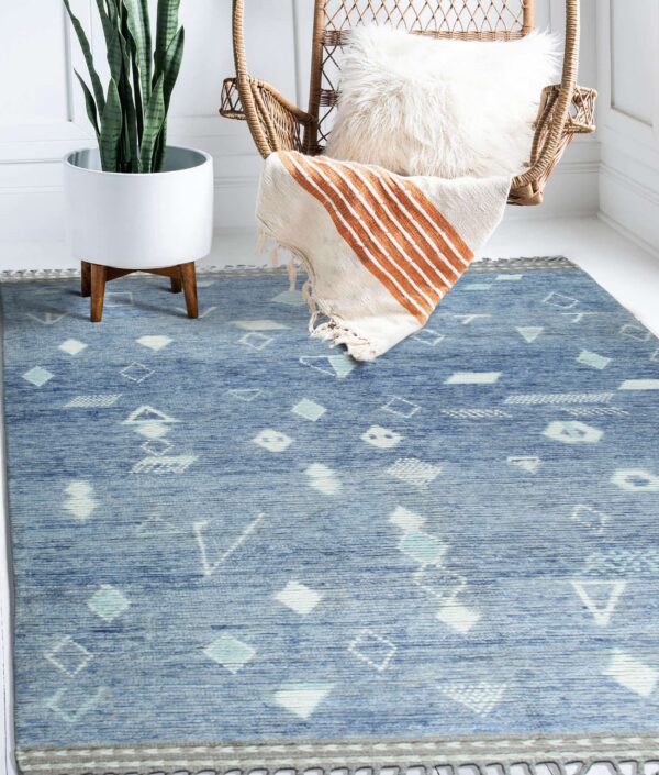 A blue rug with white and teal geometric patterns lies beneath a wicker chair and potted plant.
