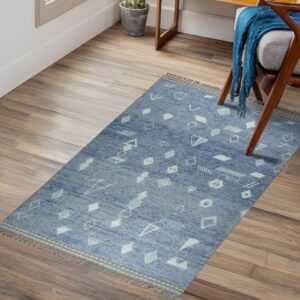 Low-pile blue geometric rug with tassels lies on wood planks beside a wooden armchair.