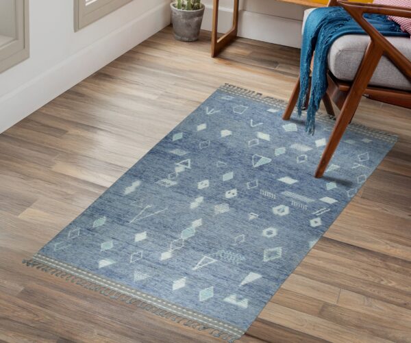 Low-pile blue geometric rug with tassels lies on wood planks beside a wooden armchair.