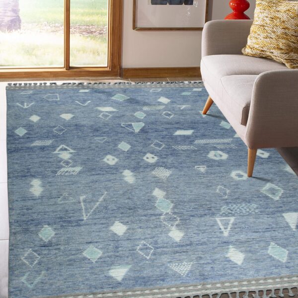 A low-pile blue rug featuring white geometric shapes sits on white tile flooring near a gray upholstered chair.