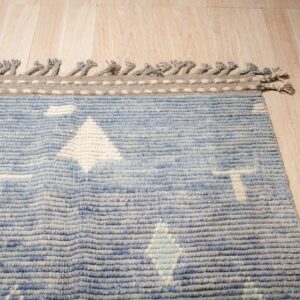 Chunky blue rug with geometric designs and tasseled edges rests on light wood plank flooring.