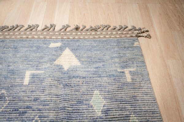 Chunky blue rug with geometric designs and tasseled edges rests on light wood plank flooring.