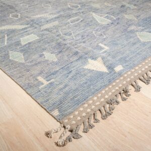 A textured blue rug featuring white geometric designs and a dotted fringe border rests on light wood flooring.