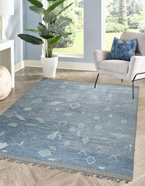 Blue geometric rug with fringe edges and abstract light blue shapes on herringbone wood floors.