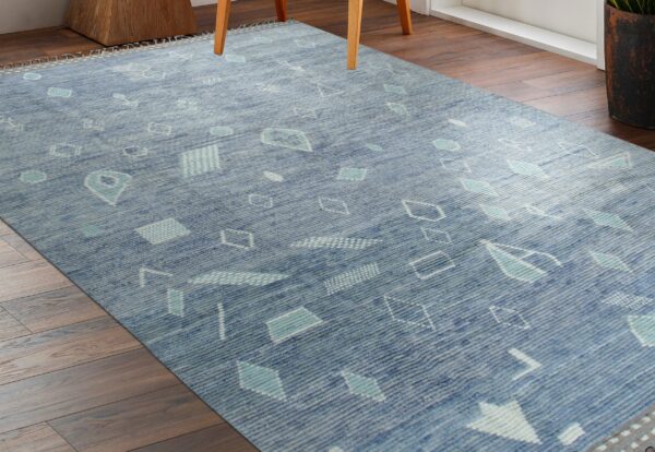 Textured blue rug with abstract turquoise and white geometric shapes rests on dark brown plank wood flooring.