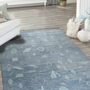 Textured blue rug with light geometric shapes and fringe anchors a bright room with grey plank flooring.