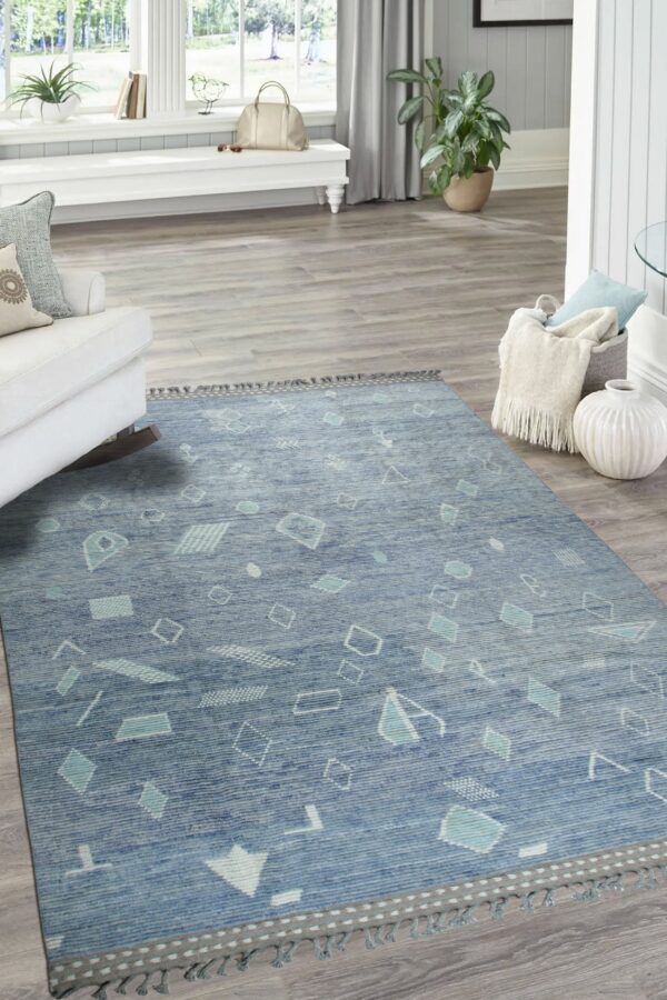 Textured blue rug with light geometric shapes and fringe anchors a bright room with grey plank flooring.