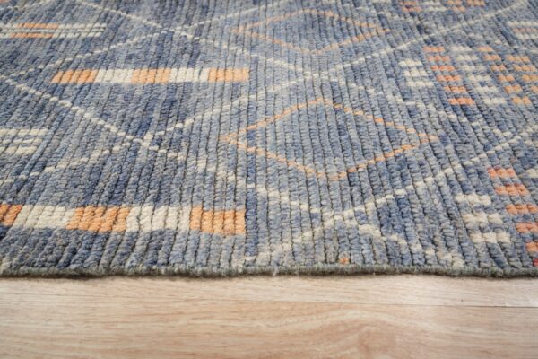 Textured blue rug showing geometric pattern in orange and white on light wood plank flooring.