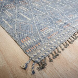 Blue geometric rug featuring white diamond patterns and orange accents rests on light wood planks.