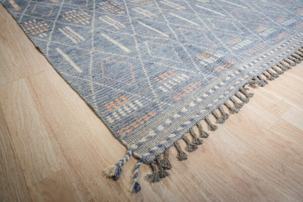 Blue geometric rug featuring white diamond patterns and orange accents rests on light wood planks.