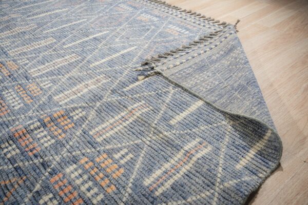 Textured blue rug with white and peach geometric pattern shown folded over on light wood flooring.