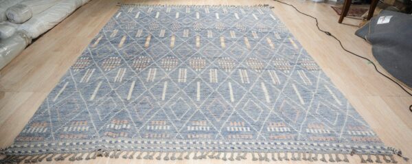Textured blue rug featuring a white diamond lattice and orange accents, displayed on light wood flooring.