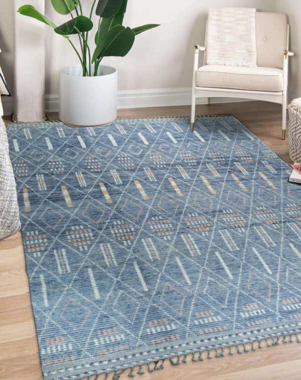 Geometric blue rug featuring white and orange patterns, visible tassels, placed beneath a beige armchair.