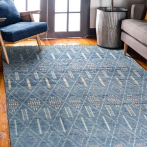 Dusty blue rug with white and peach tribal geometric patterns sits on hardwood near a blue armchair.