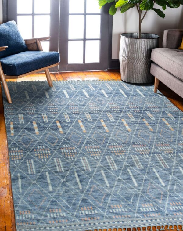 Dusty blue rug with white and peach tribal geometric patterns sits on hardwood near a blue armchair.