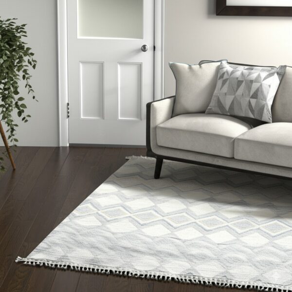 White and gray low-pile geometric rug with fringe partially under a cream sofa on dark wood.