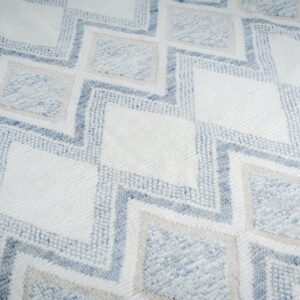 Textured rug with a geometric zigzag pattern in white, light blue, and pale tan colors.