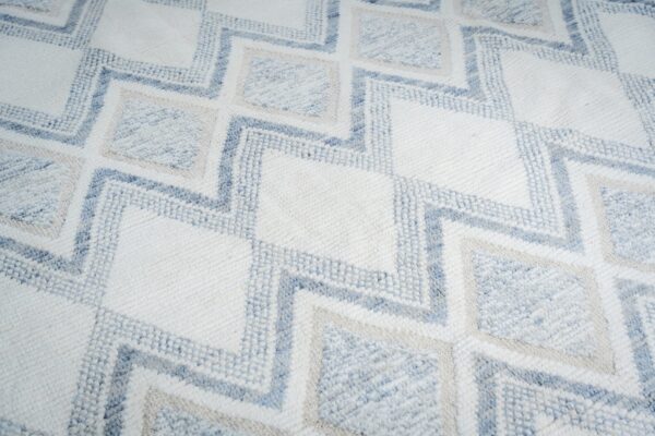 Textured rug with a geometric zigzag pattern in white, light blue, and pale tan colors.