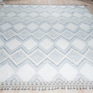 White rug with large geometric blue and tan diamonds and gray fringe, laid on wood flooring.