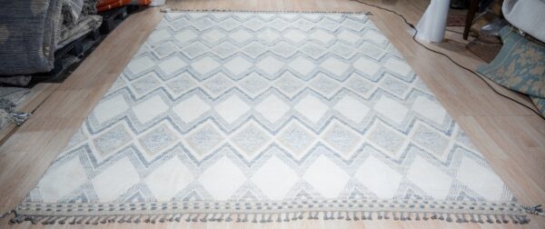 White rug with large geometric blue and tan diamonds and gray fringe, laid on wood flooring.