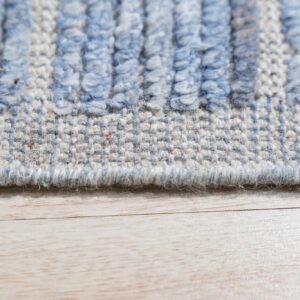 Close-up of a blue and beige striped high-low textured rug lying on light wood planks.
