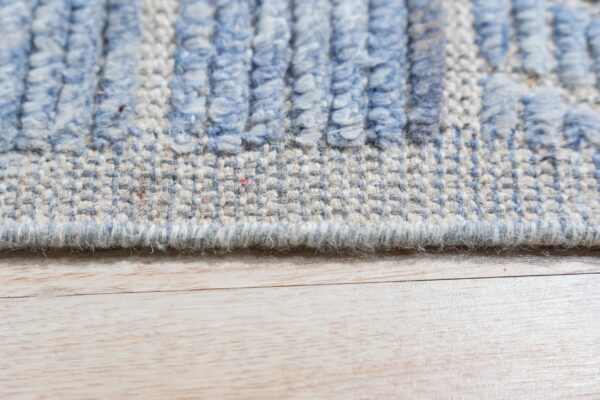 Close-up of a blue and beige striped high-low textured rug lying on light wood planks.