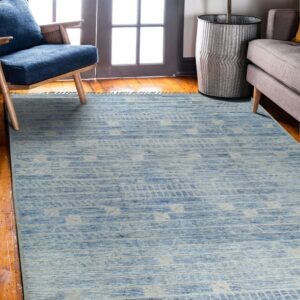 Light blue geometric-patterned rug lies on a wood floor near a window, blue chair, and grey couch.