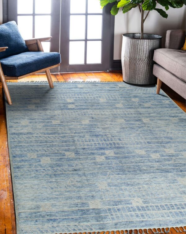 Light blue geometric-patterned rug lies on a wood floor near a window, blue chair, and grey couch.