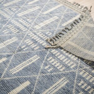 Textured blue and cream rug with a geometric pattern, folded over on a light wood floor.