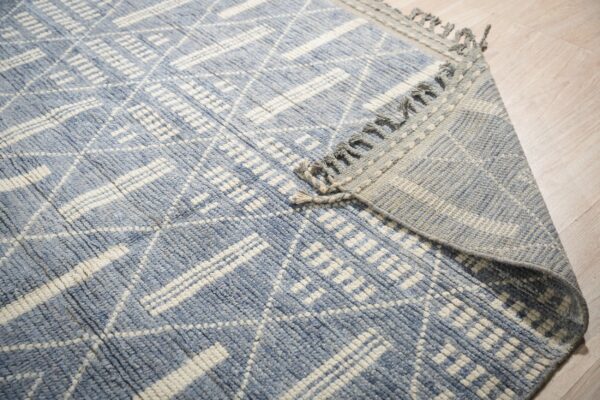Textured blue and cream rug with a geometric pattern, folded over on a light wood floor.