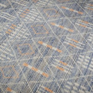 Mottled blue and gray textured rug featuring abstract geometric designs in white and light orange over wood flooring.