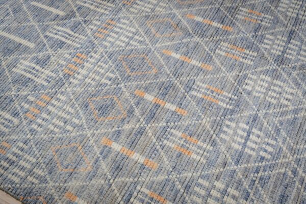 Mottled blue and gray textured rug featuring abstract geometric designs in white and light orange over wood flooring.