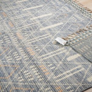 Close-up of a blue and cream textured rug with a subtle peach geometric pattern on light wood flooring.