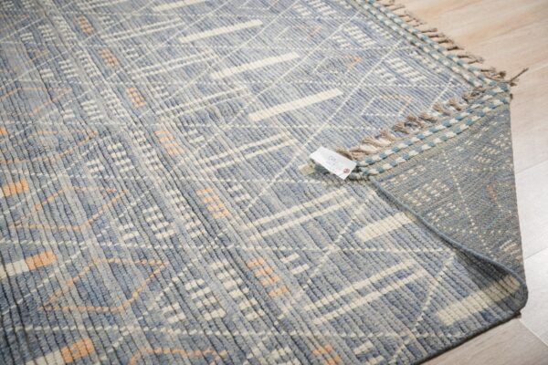 Close-up of a blue and cream textured rug with a subtle peach geometric pattern on light wood flooring.