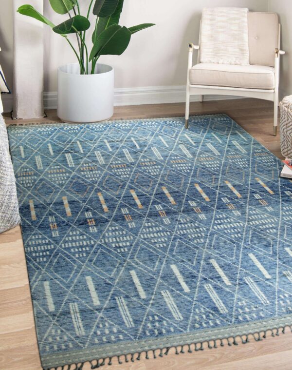 Blue rug featuring tribal geometric diamonds and dashes sits on wood flooring beside a white armchair and potted plant.