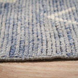 Close up of a blue and beige textured rug edge lying on light brown wood flooring.