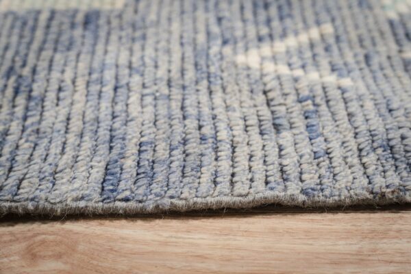 Close up of a blue and beige textured rug edge lying on light brown wood flooring.