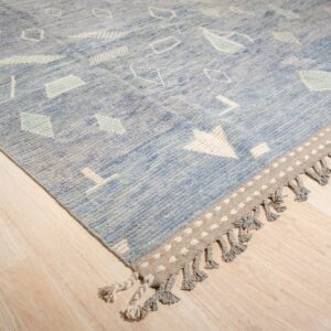 Blue textured rug with white abstract motifs and a gray tasseled border on light wood flooring.
