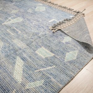 A geometric blue, white, and mint low-pile rug with fringe detailing is visible on light wood plank flooring.